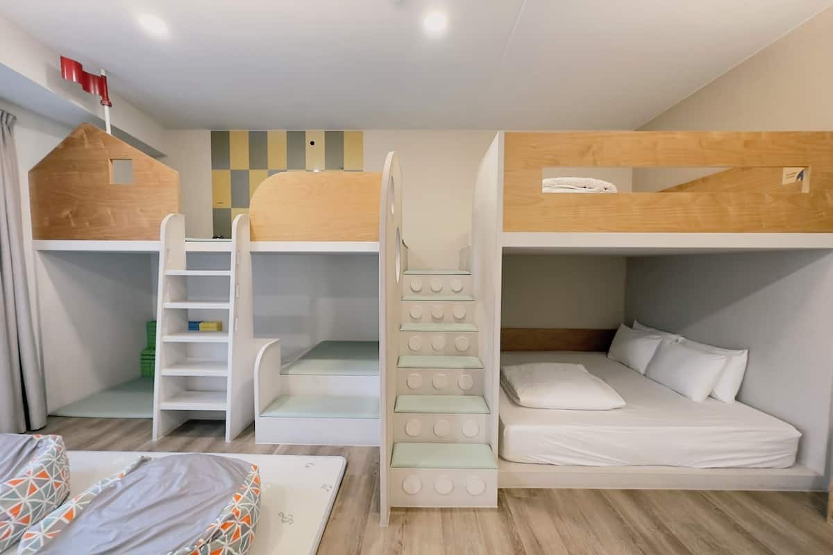 A bunk bed room with a ladder, a small playhouse, and a bed with pillows.