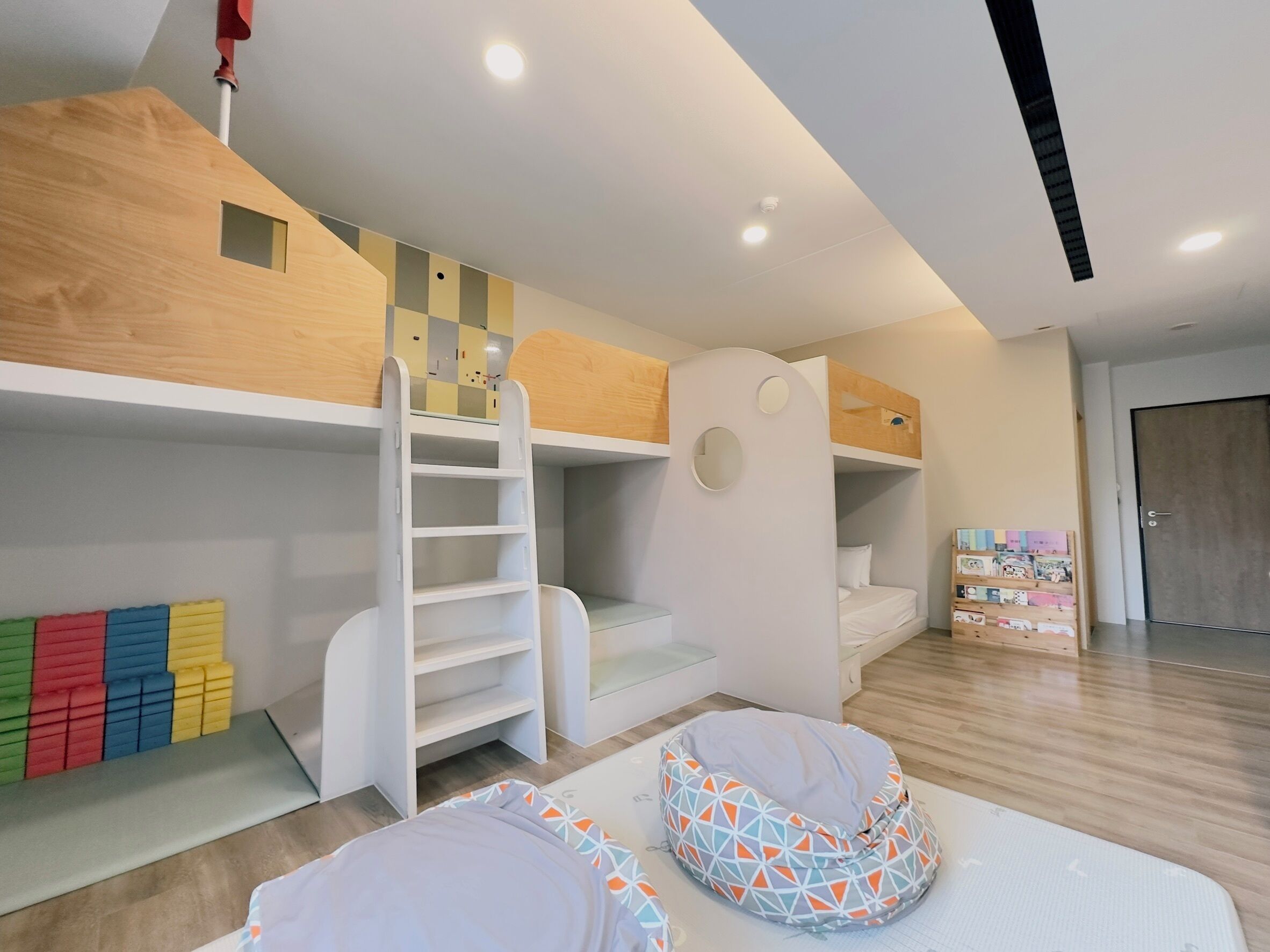 A children's room with bunk beds, a ladder, colorful foam blocks, and a bean bag chair.