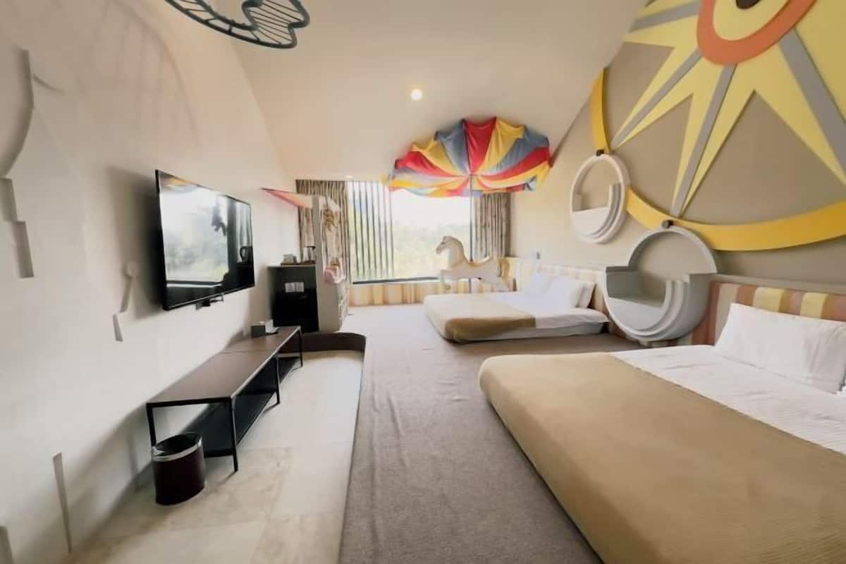 A hotel room with a bed, a TV, a desk, and a large window.