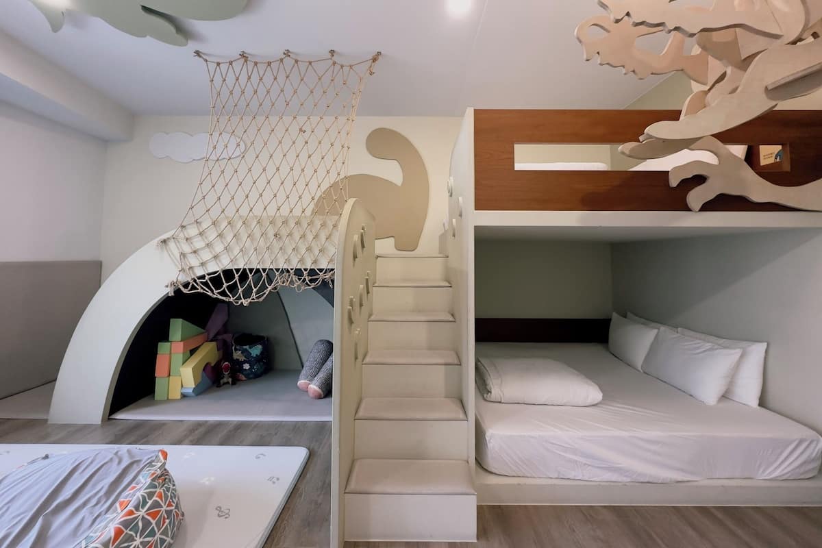 A bunk bed room with a netted play area, a staircase, and a unique ceiling design.