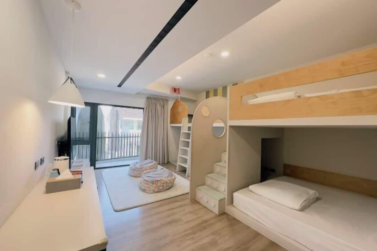 A modern hotel room with a bunk bed, a desk with a lamp, a small seating area, and a staircase.