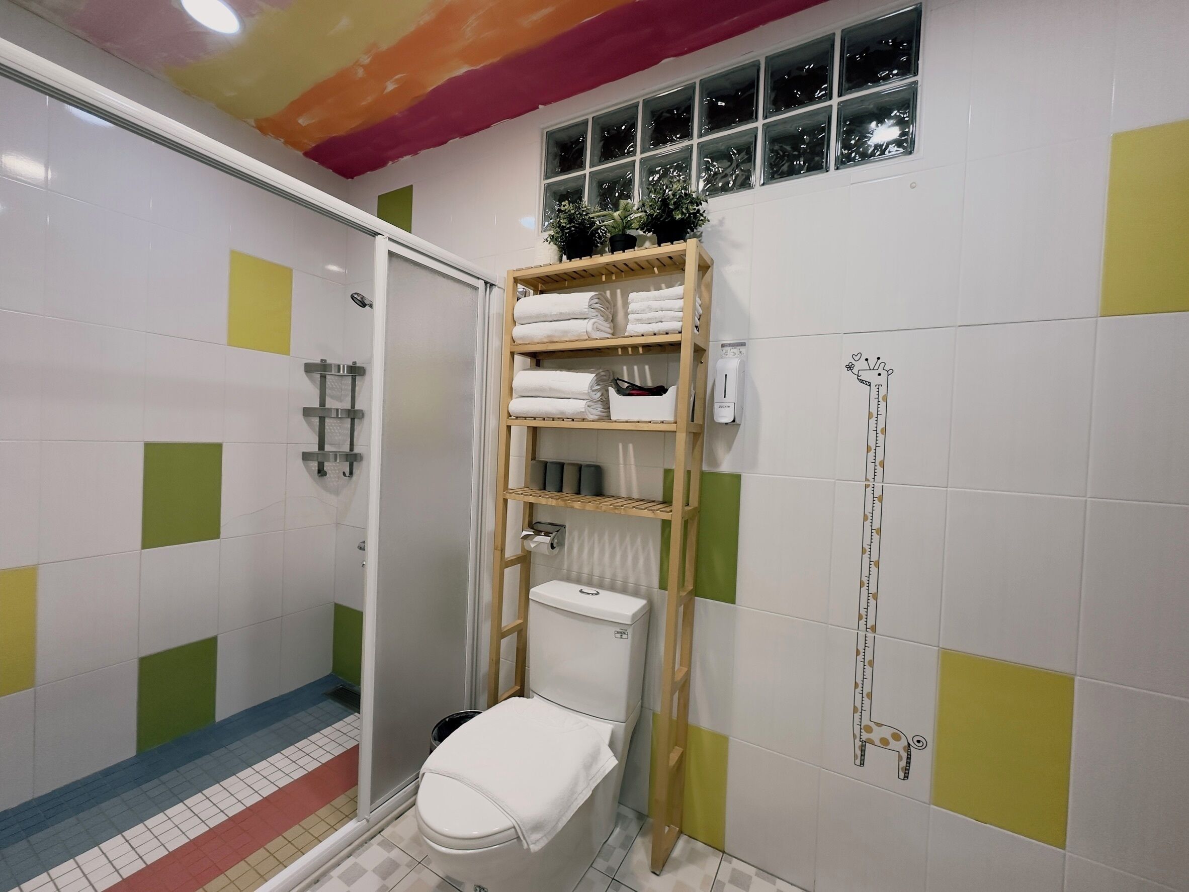 A bathroom with a toilet, a shower, a wooden shelf with towels, a hand dryer, and a window with a view.