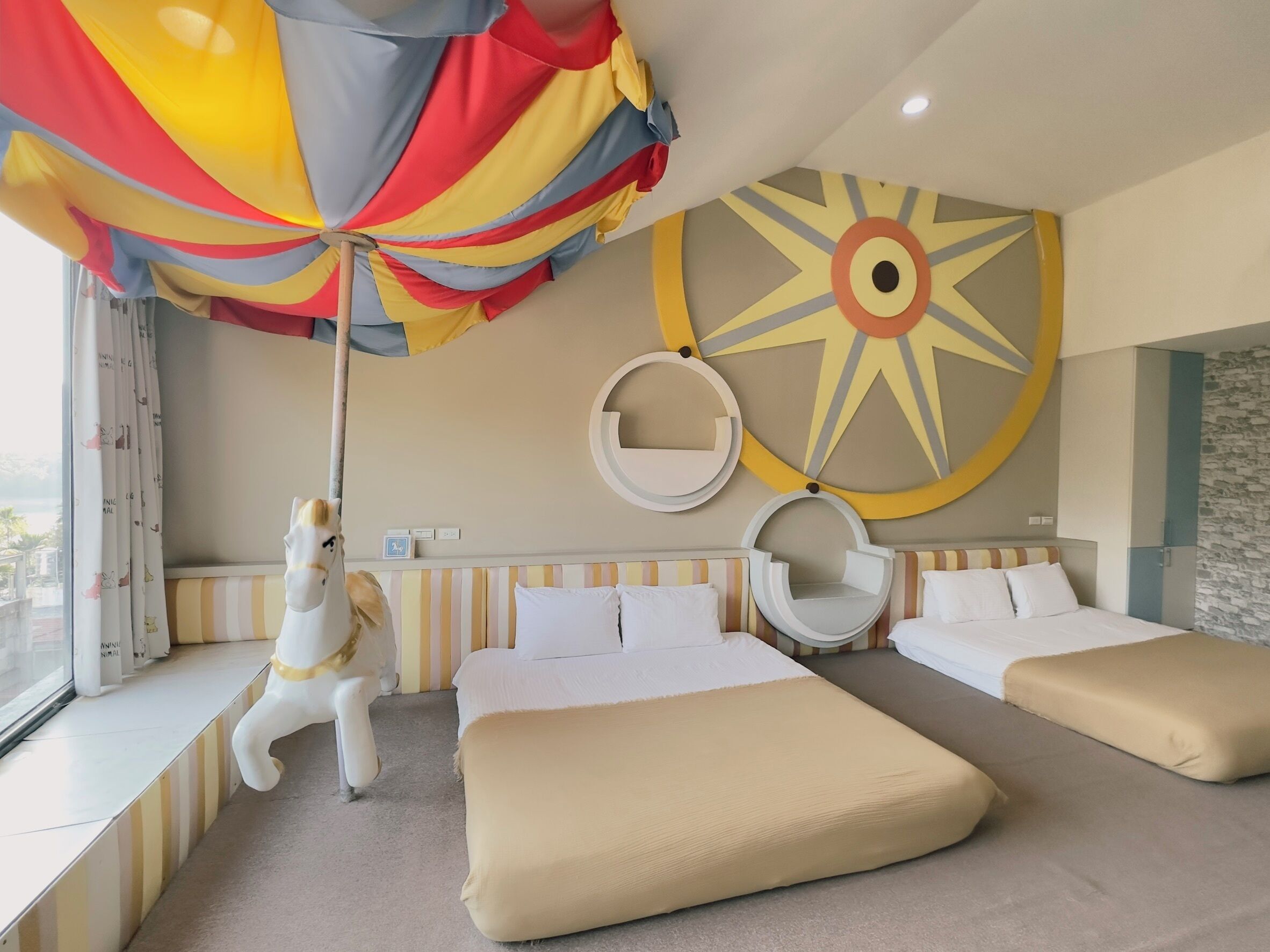 Una camera d'albergo con due letti, una grande decorazione a parete simile al sole e una poltrona sospesa.