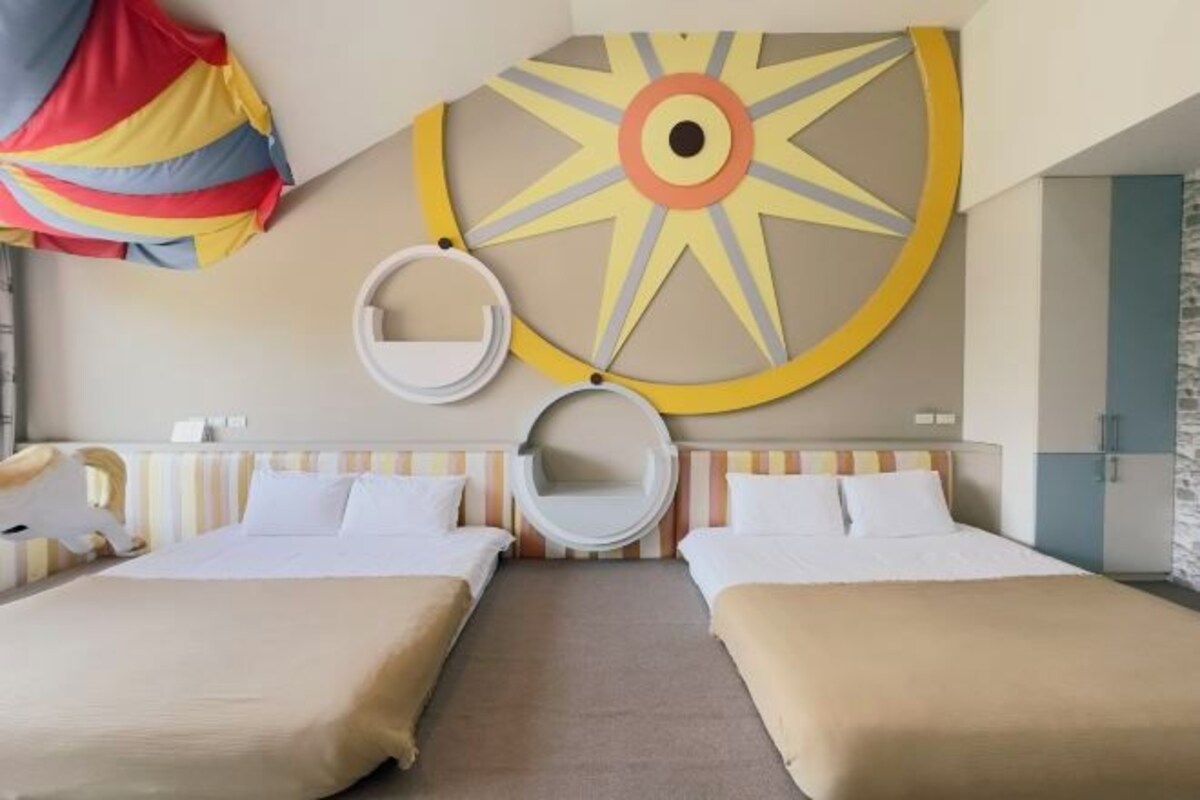 Habitación de hotel con dos camas, una gran decoración en la pared con forma de sol y dos sillas colgantes circulares.