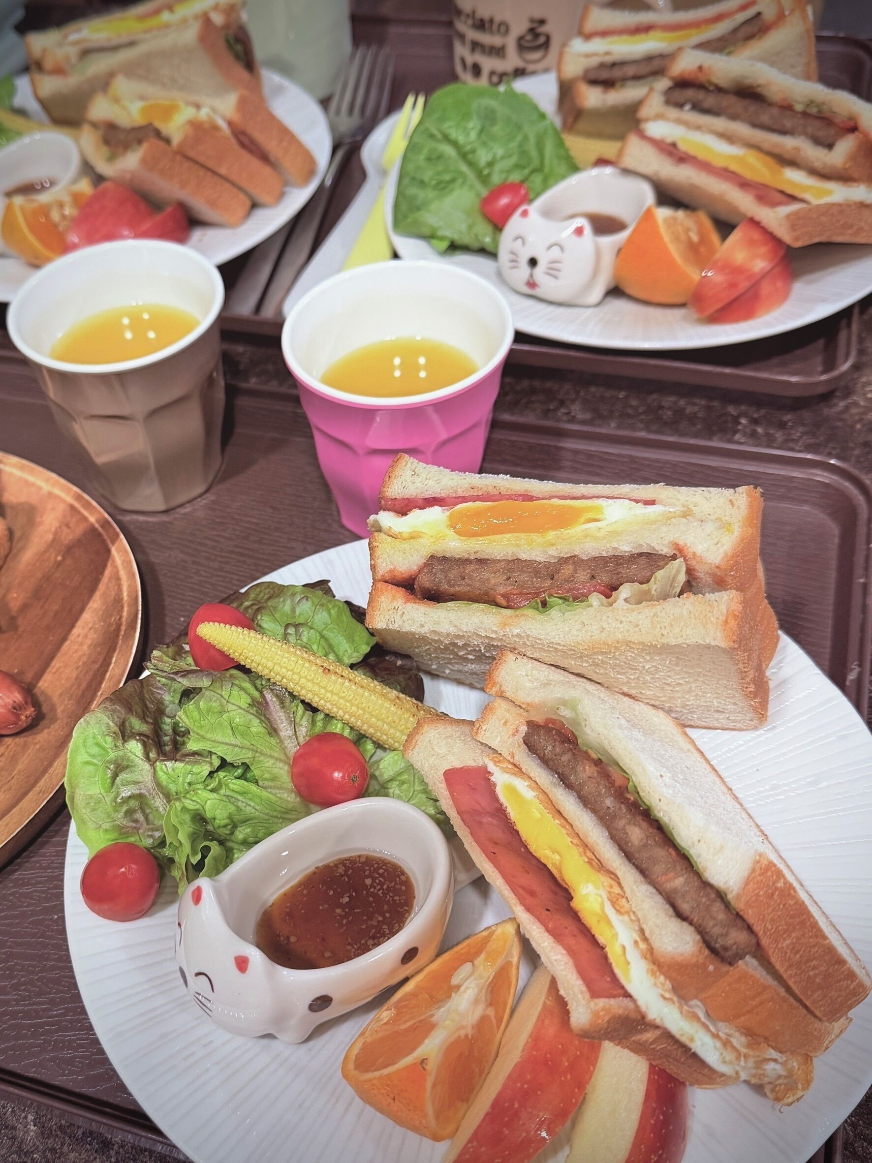 A table with sandwiches, fruits, and a small ceramic cup.