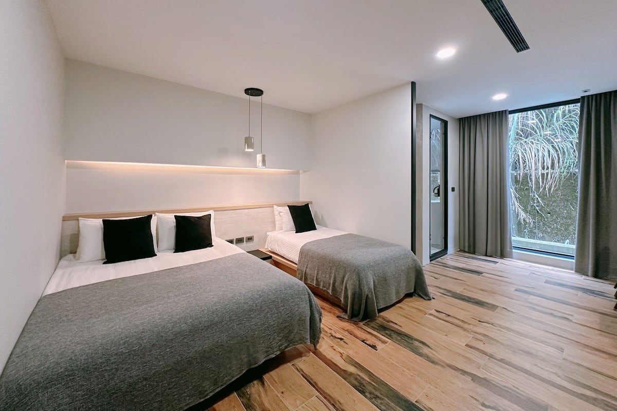 A modern hotel room with two beds, a large window with curtains, and a wooden floor.