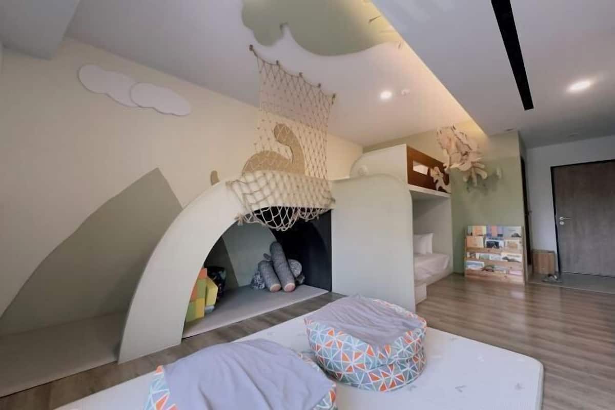 A children's play area with a netted climbing structure, a soft play mat, and a loft bed.