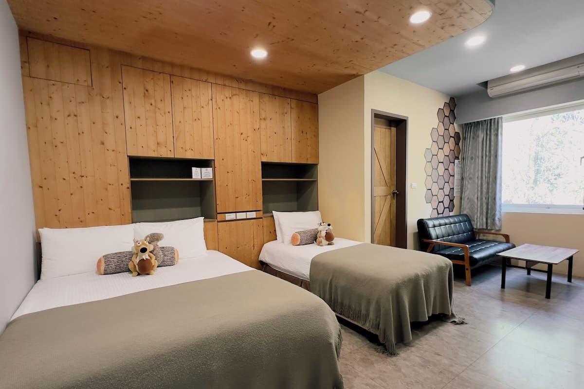 A hotel room with two beds, a sofa, a small table, wooden paneling on the walls, and a window with curtains.