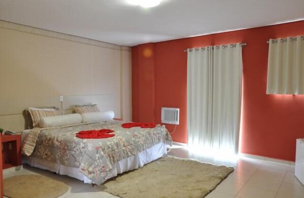 Relax in a spacious bedroom with a large bed, bedside table, and window with white curtains.
