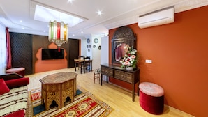 A living room with a wooden coffee table, a sofa, a red ottoman, a chandelier, and a decorative mirror. - PMC Business Apartments (Ruesselsheim)