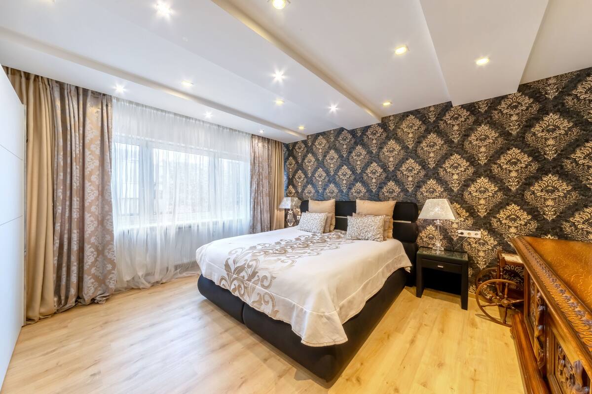 Quarto com cama grande, mesa de cabeceira, abajur e cadeira de madeira.