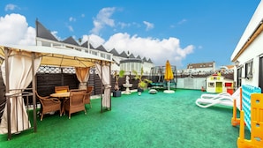 A covered outdoor seating area with wicker furniture, a small fountain, and a play structure. - PMC Business Apartments (Ruesselsheim)