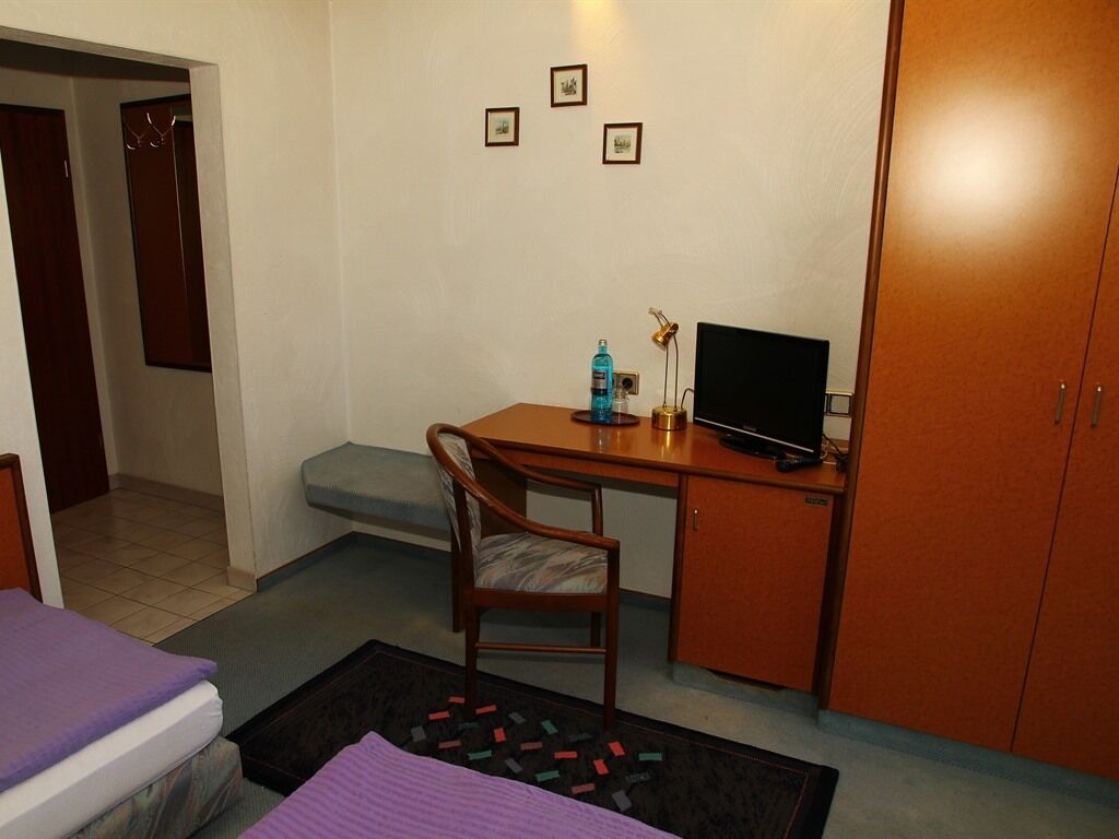 Ein kleines Hotelzimmer mit einem Bett, einem Schreibtisch mit Computer, einem Sessel und einem Kleiderschrank.