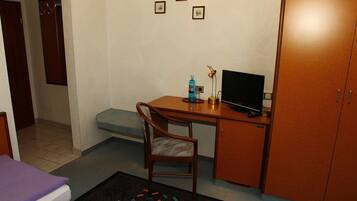 Ein kleines Hotelzimmer mit einem Bett, einem Schreibtisch mit Computer, einem Sessel und einem Kleiderschrank.