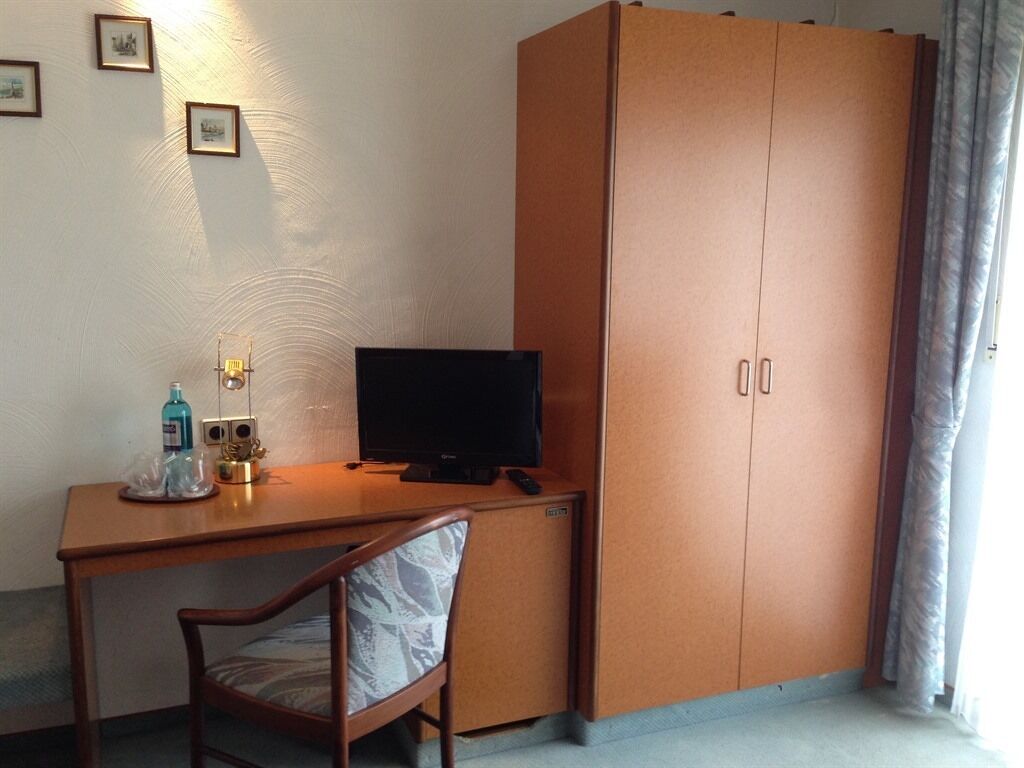 A room with a wooden desk, a television, a chair, and a wardrobe.