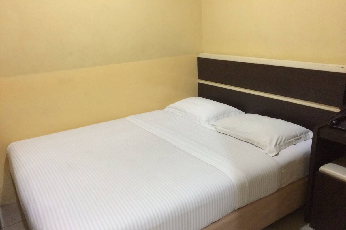 A small, single-bed room with a plain white bedspread and a dark headboard.