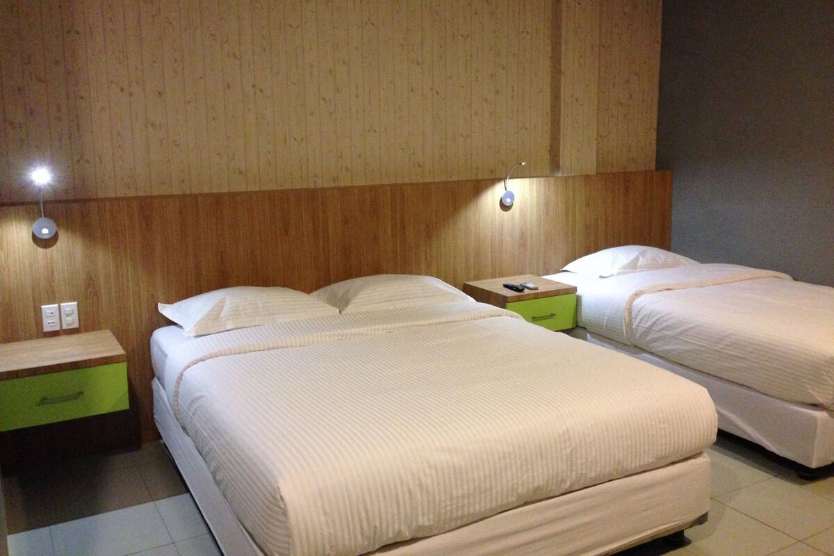 A hotel room with two beds, wooden headboard, bedside tables with lamps, and a green drawer.