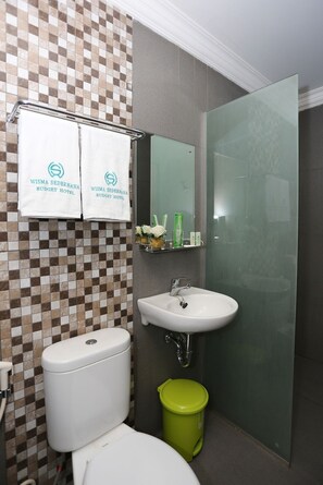 A bathroom with a tiled backsplash, a white sink, a toilet, and a green trash bin. - Wisma Sederhana Budget Hotel (Medan)