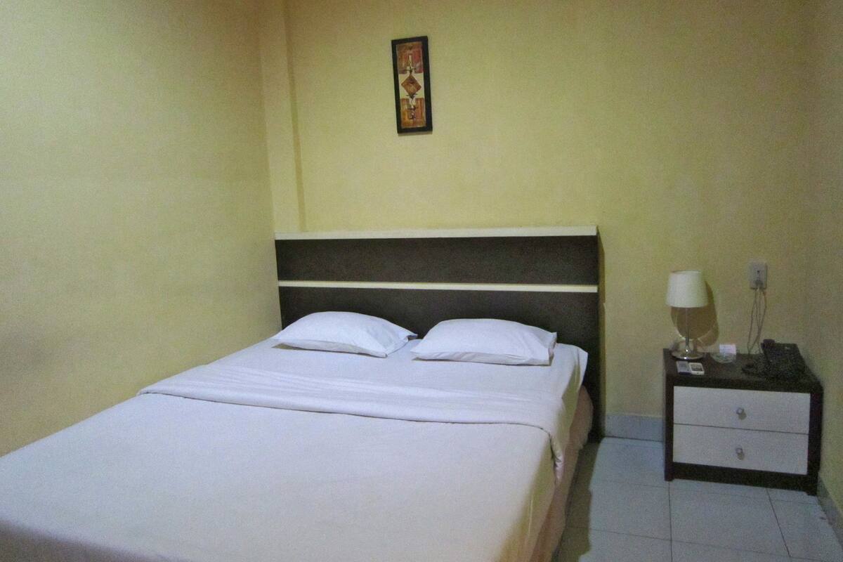 A single bed with white bedding, a nightstand with a lamp, and a small picture on the wall.