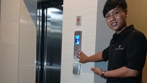 Een persoon staat naast een lift met een bedieningspaneel en een digitaal scherm.