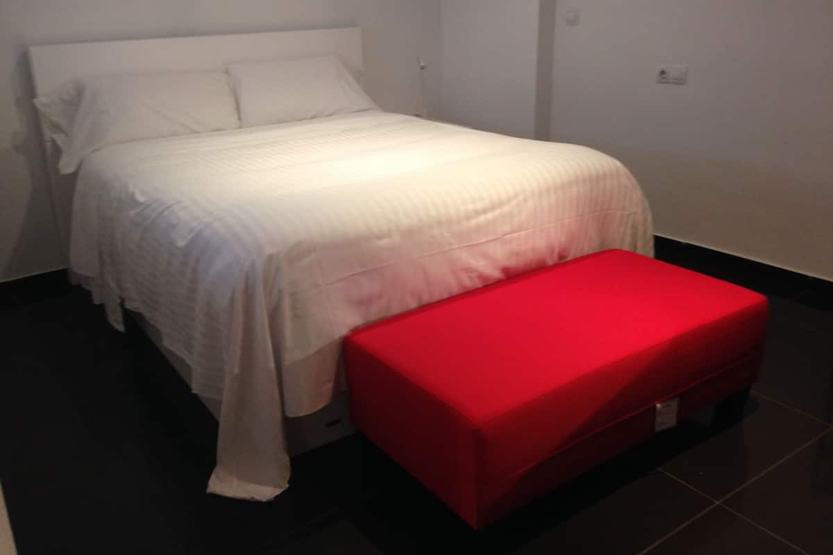 Una cama con ropa de cama blanca y un banco rojo.