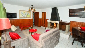 Una sala de estar con chimenea, un sofá, un sillón rojo, un televisor y un aparador de madera.