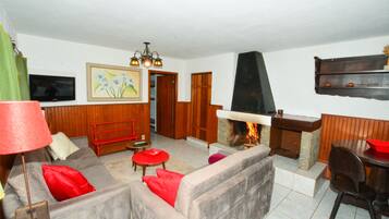 Uma sala de estar com lareira, um sofá, uma poltrona vermelha, uma televisão e um armário de madeira.