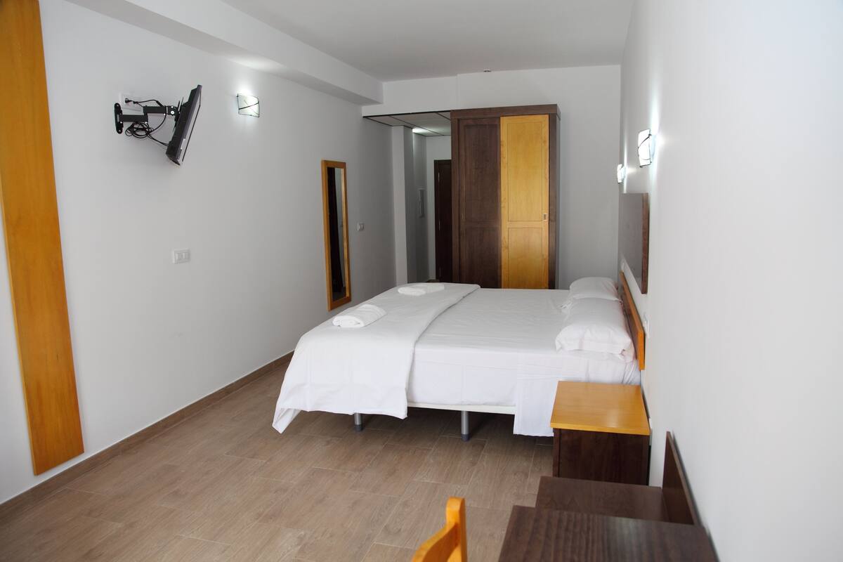 A bedroom with a bed, a wooden desk, a chair, and a mirror.
