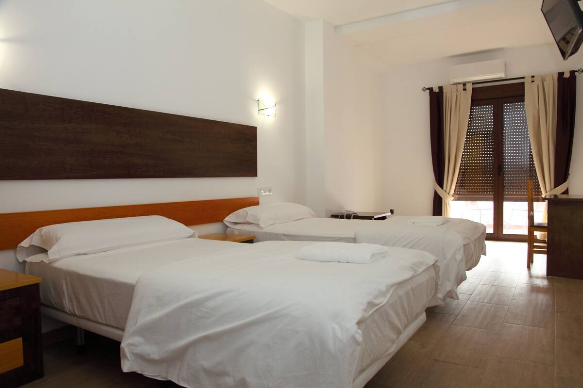 A hotel room with two beds, a wooden headboard, a flat-screen TV, and a window with curtains.