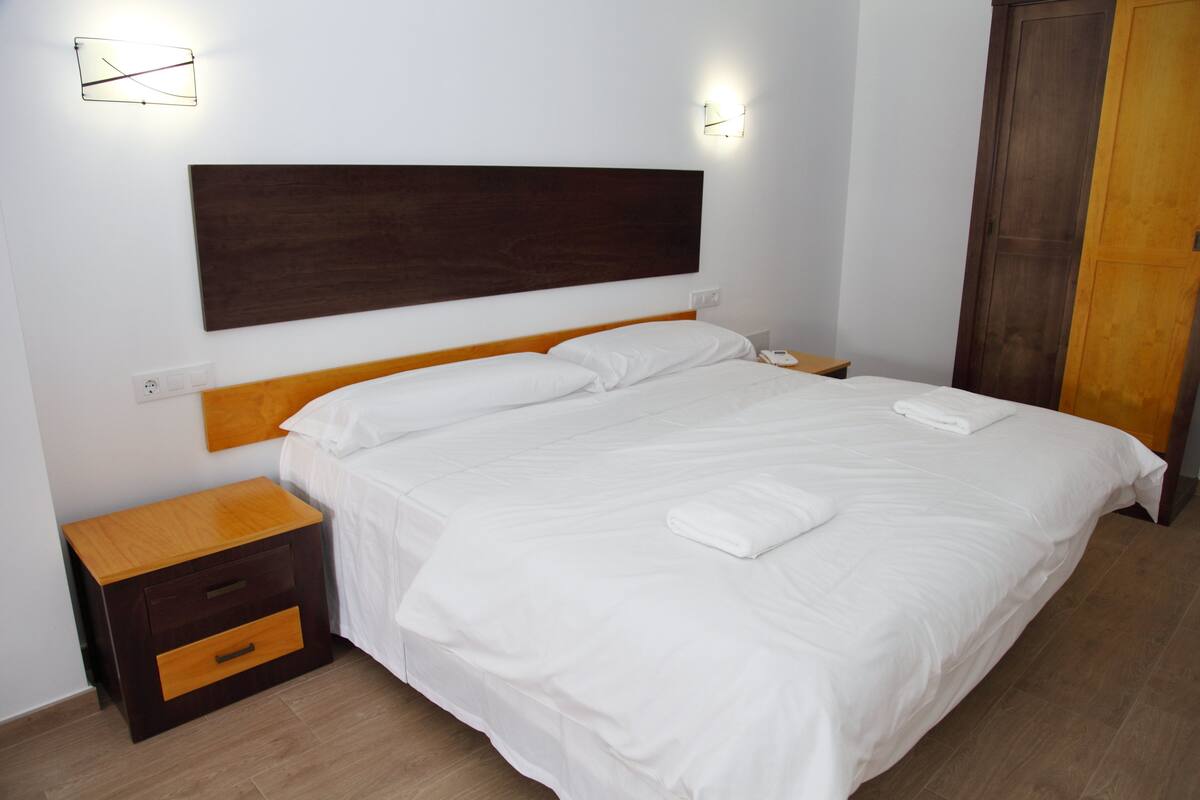 A neatly made bed with white linens, a wooden headboard, and a nightstand with a drawer.