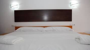 Una cama bien hecha con sábanas blancas, cabecera de madera y dos lámparas fijadas a la pared.