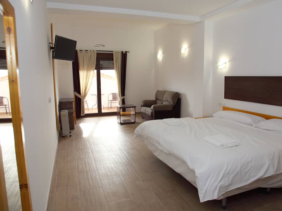 Habitación de hotel con una cama grande, una silla, un escritorio con computadora y un televisor en la pared.