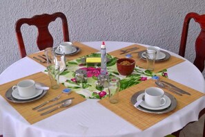 A round dining table with a white tablecloth, set with white cups, saucers, cutlery, and a glass pitcher. - Pousada Vó Irene (Mangaratiba)