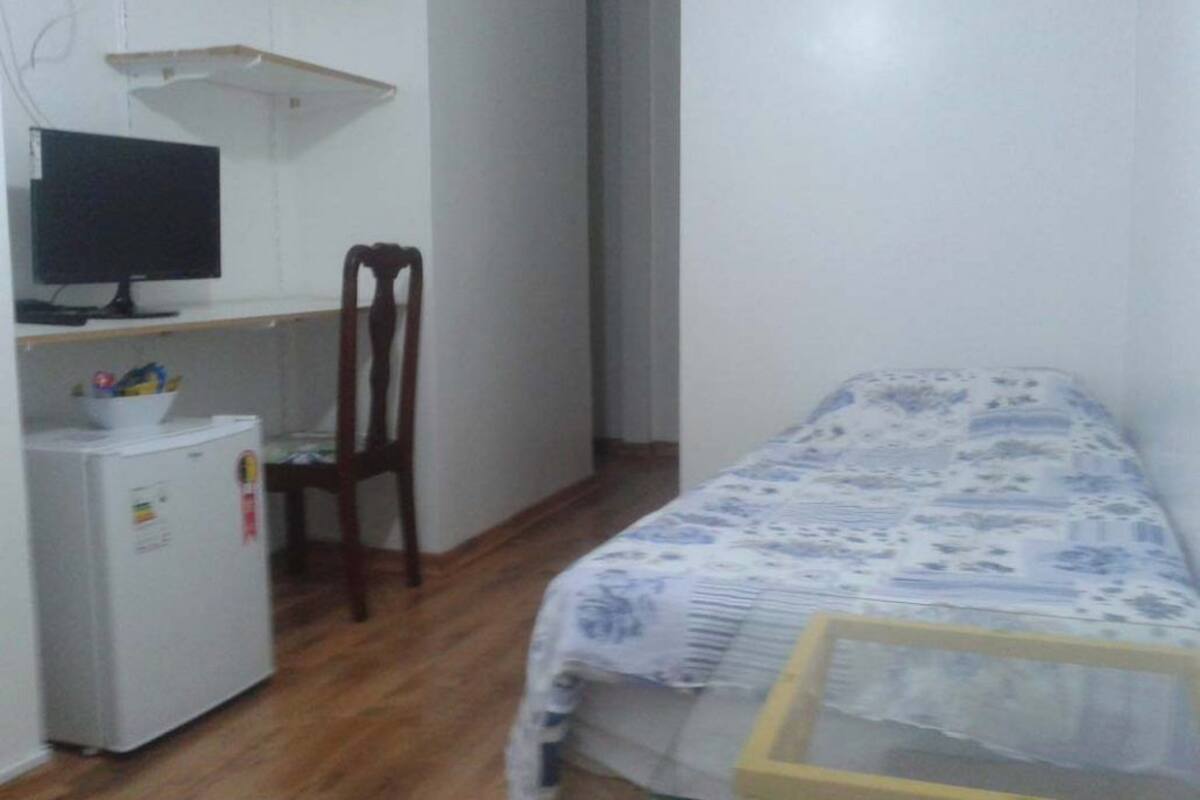 A bedroom with a bed, a desk with a computer, and a small refrigerator.