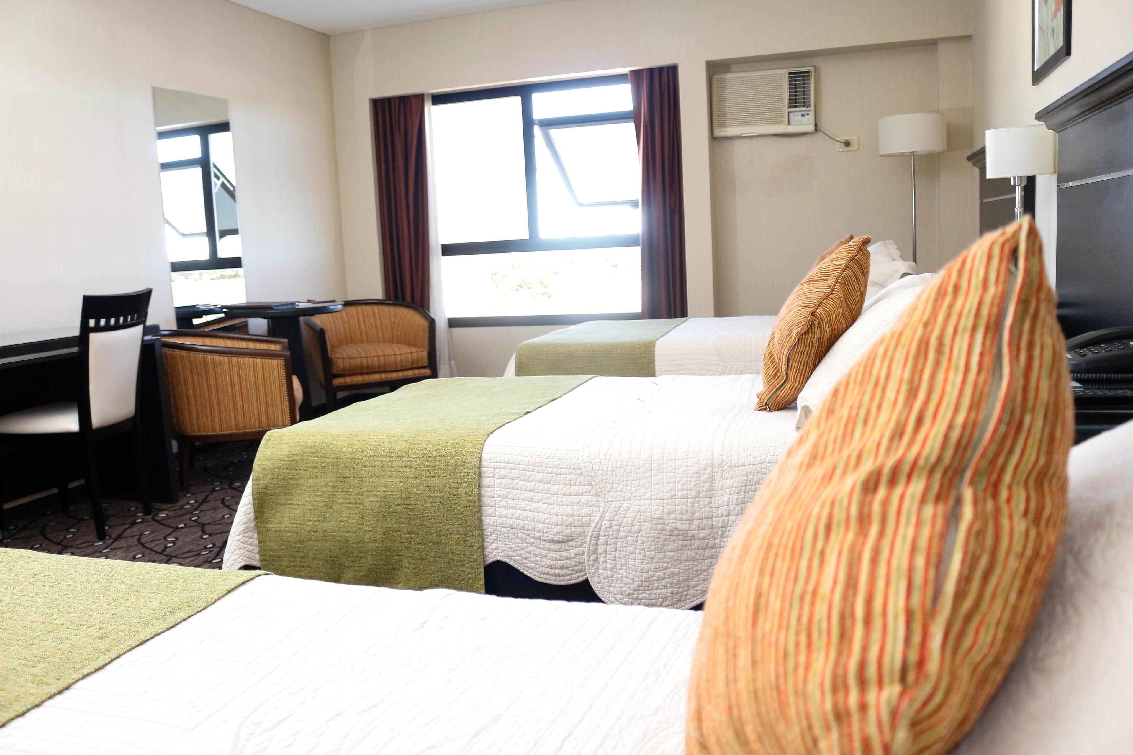 A hotel room with two beds, a desk, a chair, and a window with curtains.