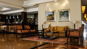 Un hall d’entrée avec un coin bar, des sièges dotés de coussins à rayures et deux tableaux représentant des paysages, encadrés et accrochés au mur.