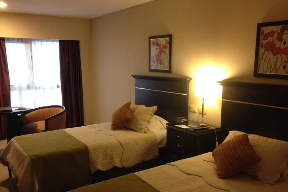 Une chambre d’hôtel avec deux lits, un bureau et une chaise. Il y a une table de chevet avec une lampe et un téléphone.