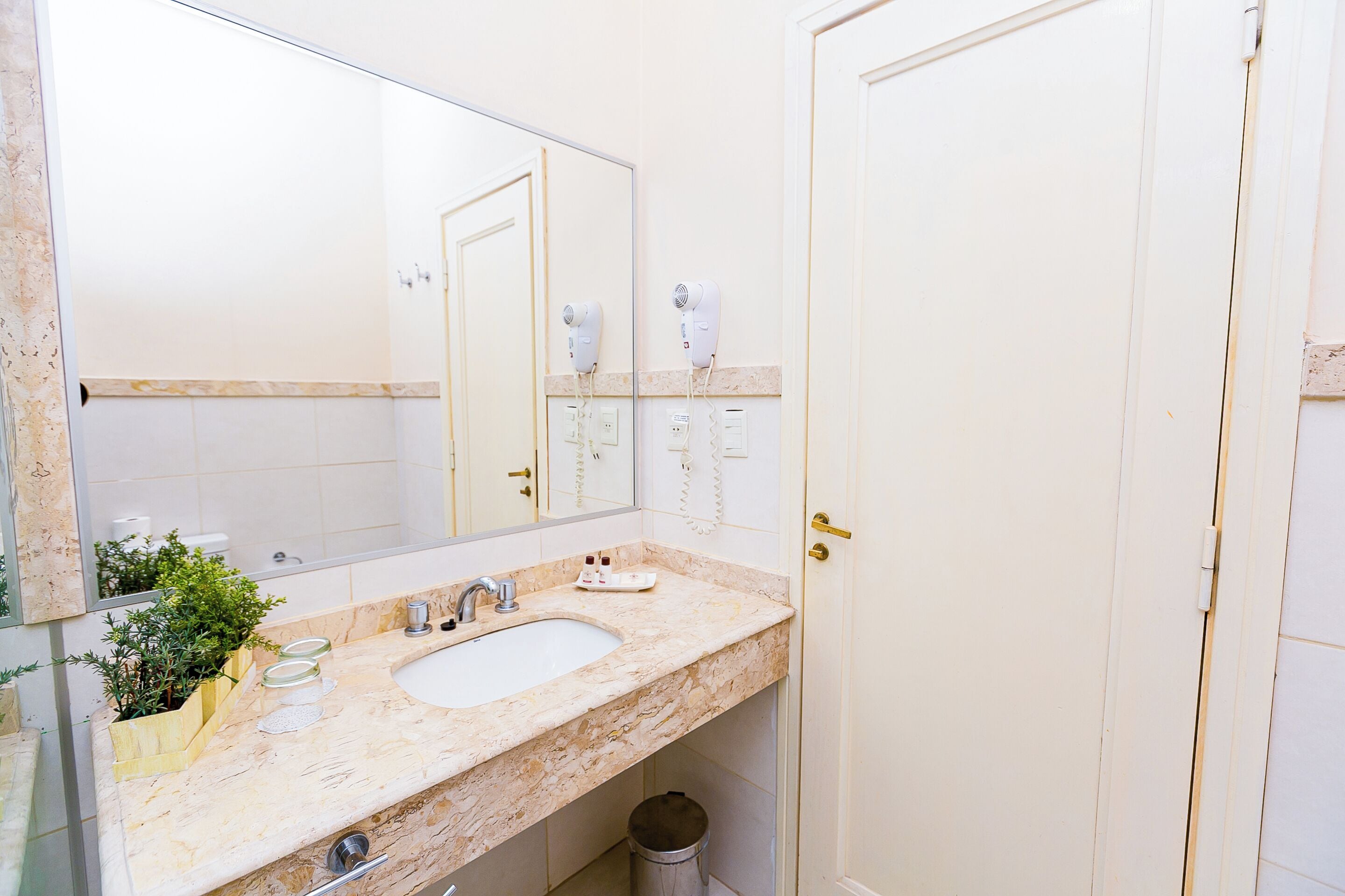 Un baño con lavamanos de mármol, espejo, secador de pelo y cubo de basura.