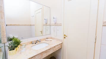 Un baño con lavamanos de mármol, espejo, secador de pelo y cubo de basura.