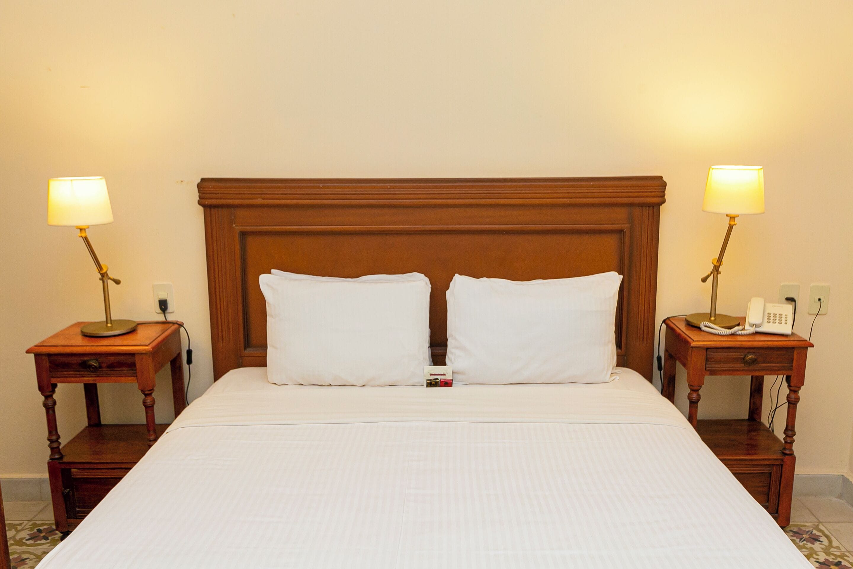 A neatly made bed with a wooden headboard, two bedside tables with lamps, and a telephone on one of the tables.