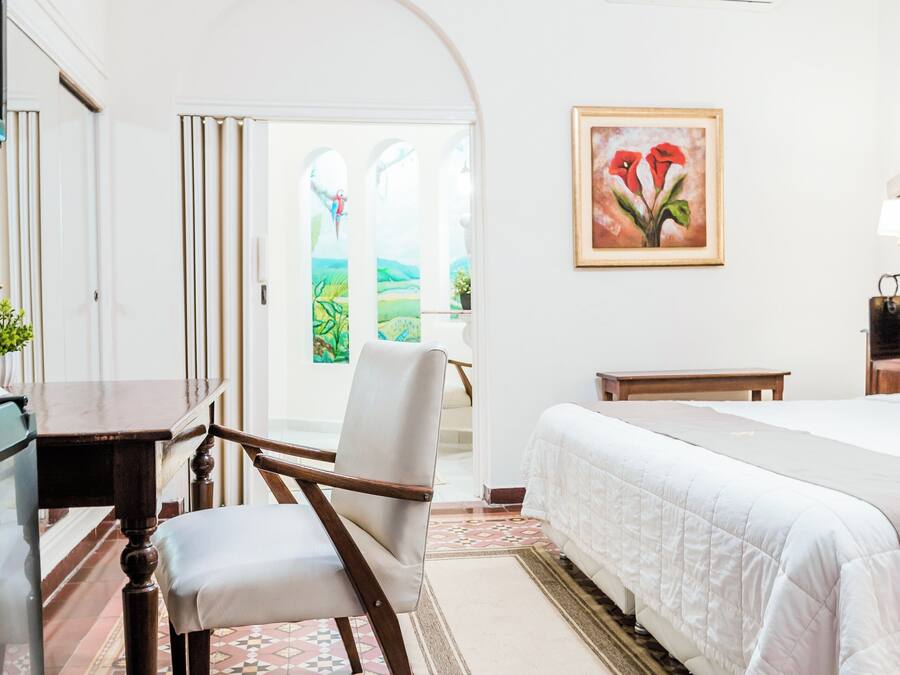 Un dormitorio con cama, escritorio, silla y un cuadro en la pared.