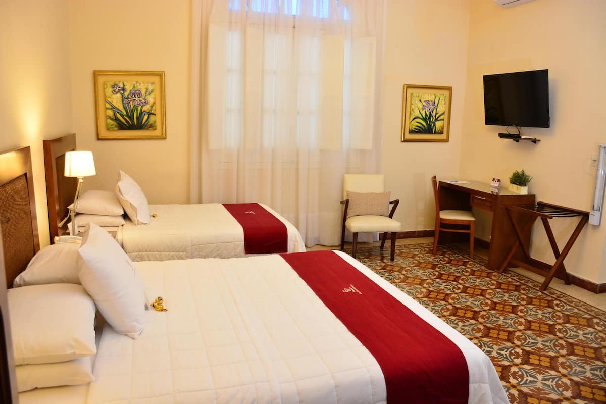 A hotel room with two beds, a desk, a chair, a television, and artwork on the walls.