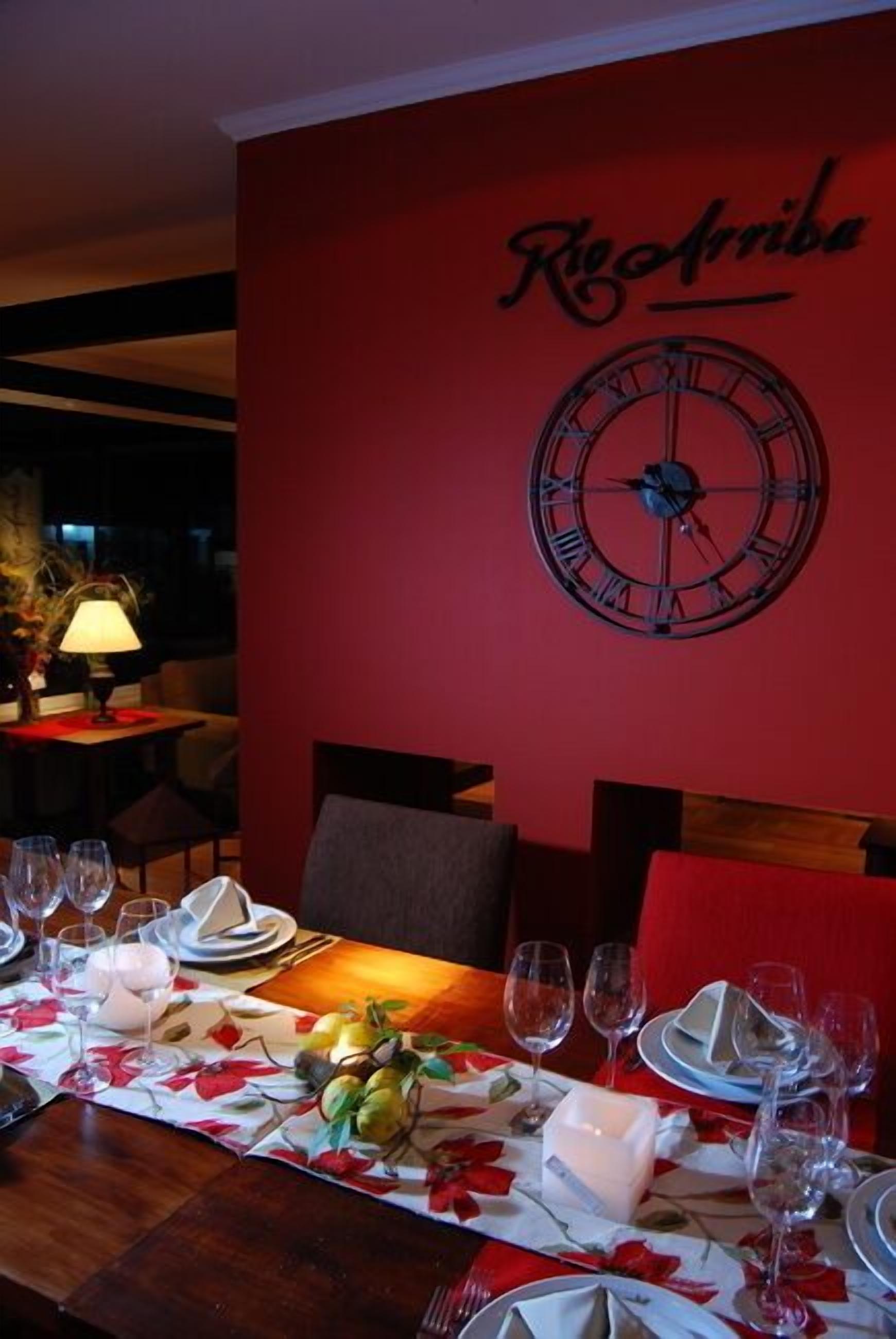 Un comedor con pared roja, un reloj y una mesa preparada para una comida.
