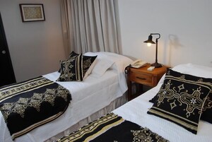 Habitación de hotel con dos camas, cada una con ropa de cama estampada y una mesita de noche con lámpara y teléfono.