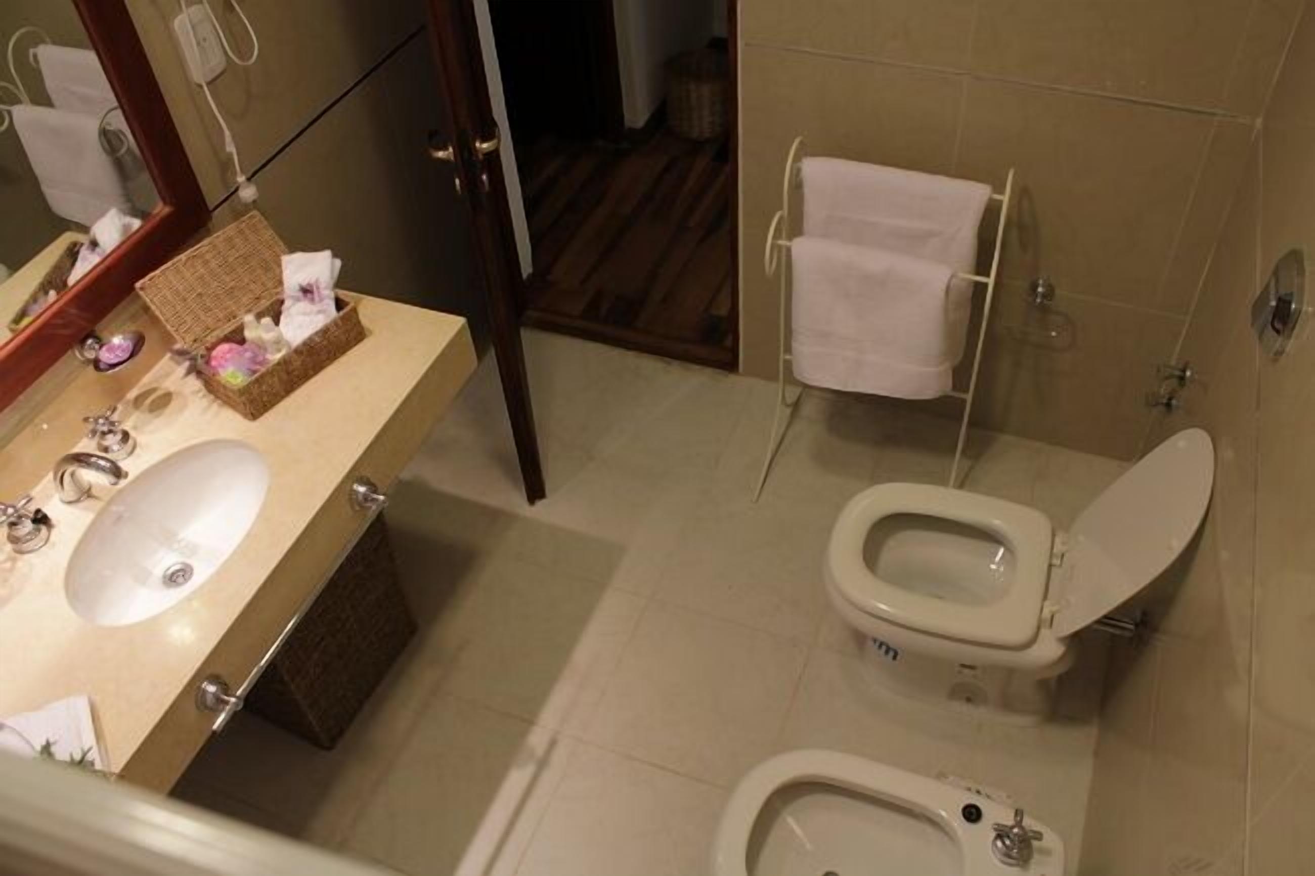 Een badkamer met een wastafel, toilet, bidet en een klein spiegel.