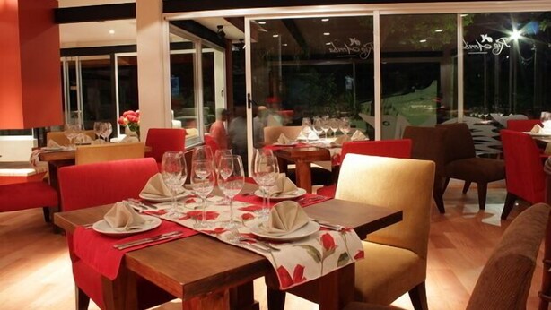 A restaurant with tables set for dining, featuring red chairs and a glass partition wall. - Rio Arriba Suites Apartments y Resto (Bella Vista)