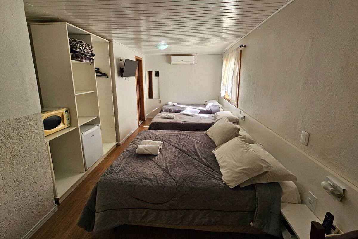 Habitación estrecha con dos camas, un armario, televisor y ventilador de techo.