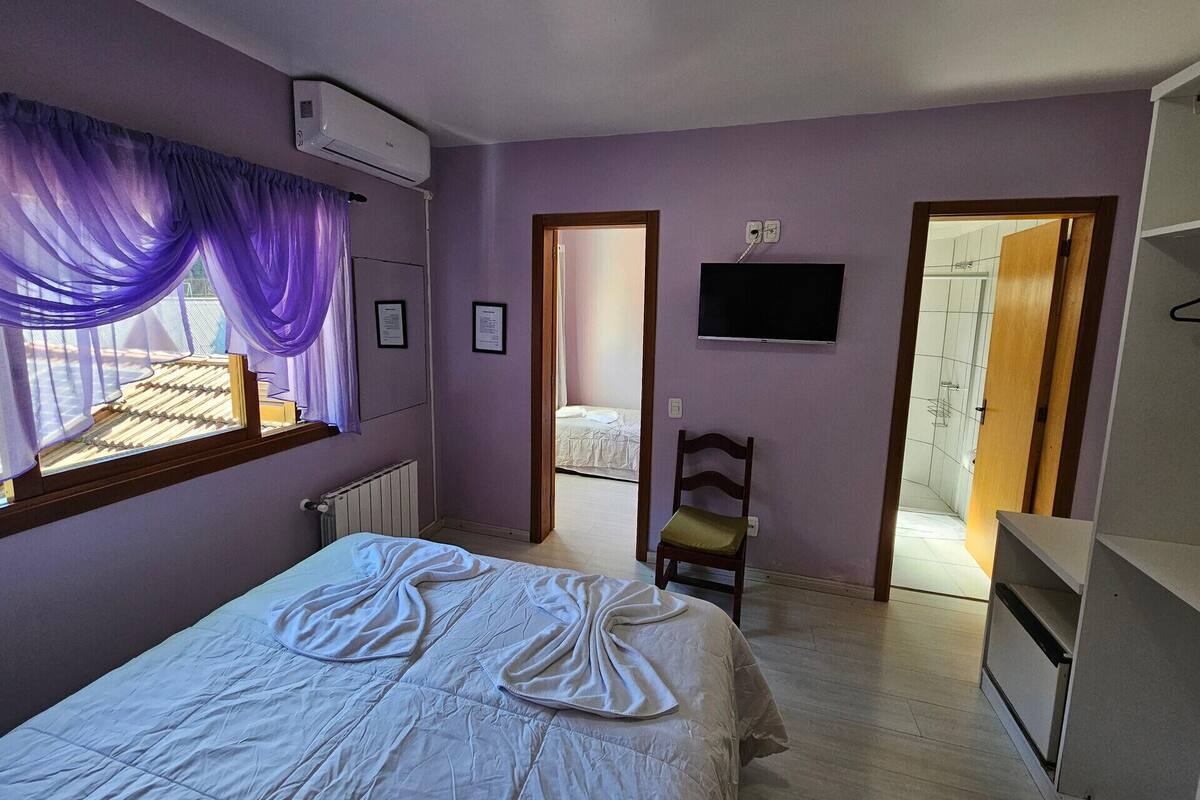 Un dormitorio con cama, una silla, un televisor y una puerta que da a otra habitación.