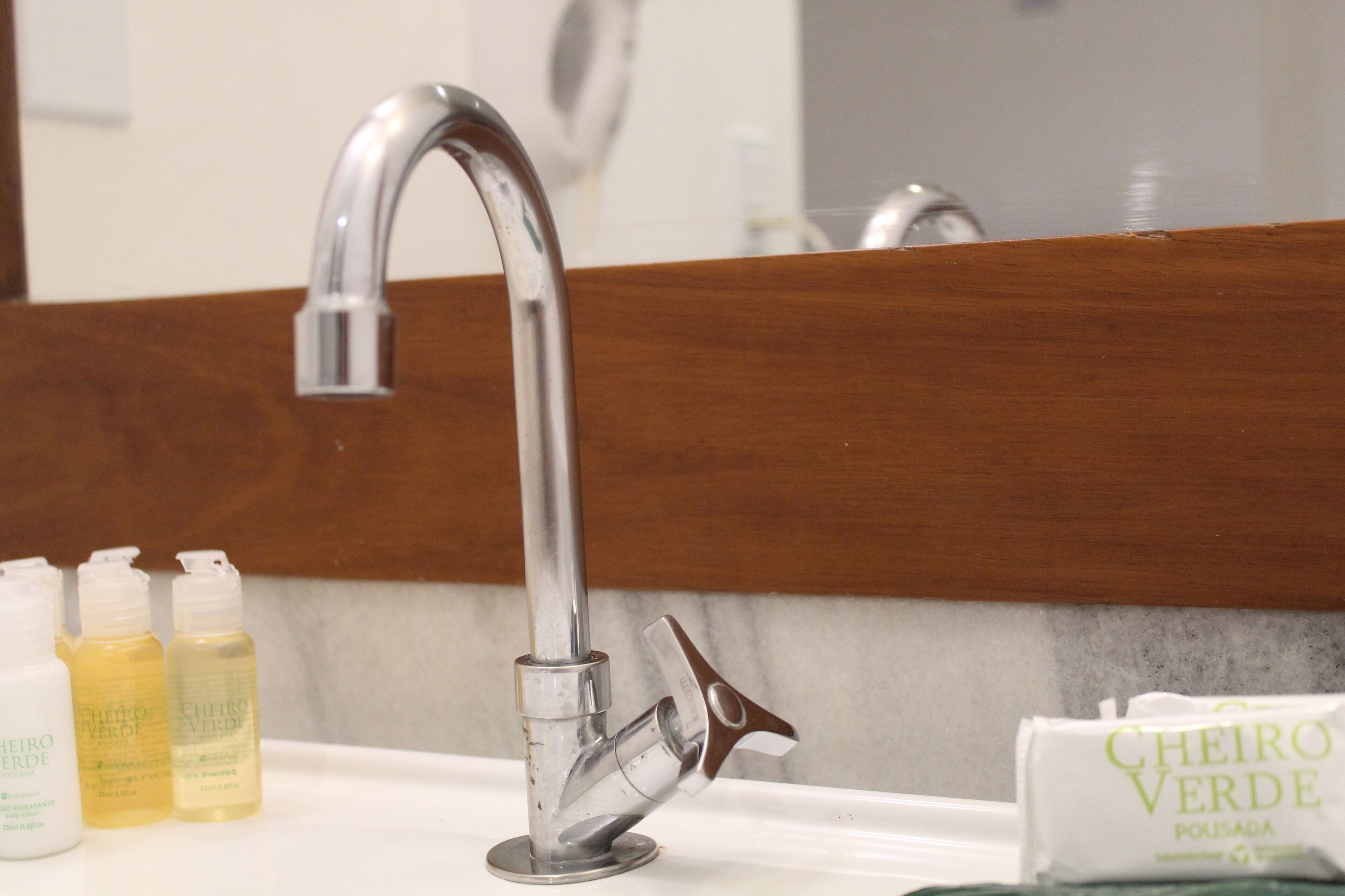 A bathroom sink with a chrome faucet, three toiletry bottles, and a package of toiletries.