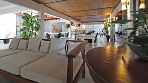 Un vaste espace de vie doté d’un plafond en bois, d’un canapé beige et de plantes en pot.
